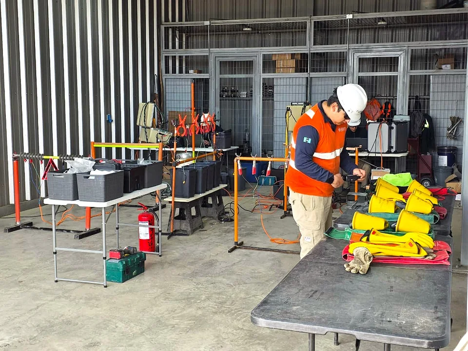 Persona con casco trabajando junto a equipos y elementos de protección en un área de trabajo.